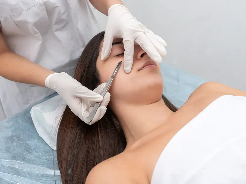 Gloved esthetician performing ultrasonic dermaplaning on a relaxed client