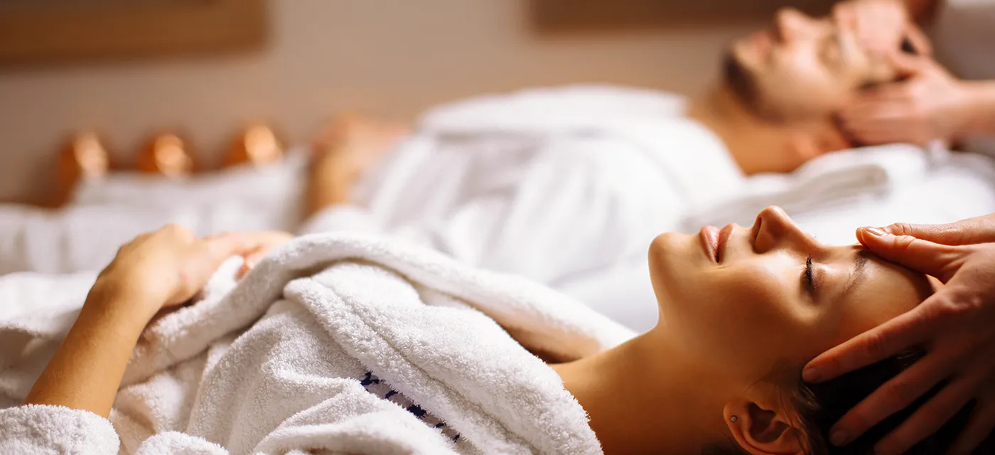 A couple receiving side-by-side facial massages in robes
