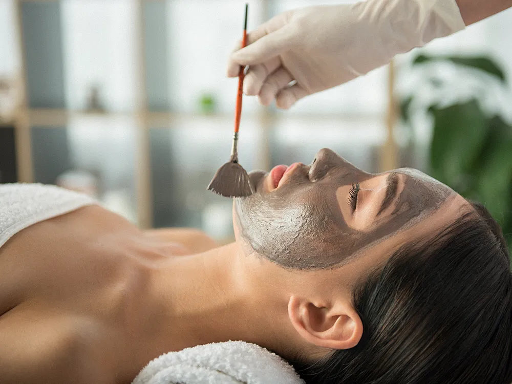 Esthetician brushing a clay mask onto a relaxed client's face